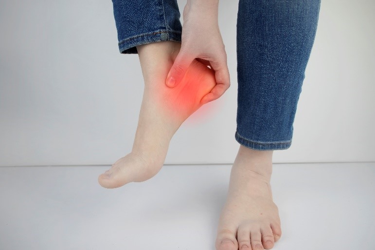 Woman holding foot experiencing heel pain from Plantar Fasciitis